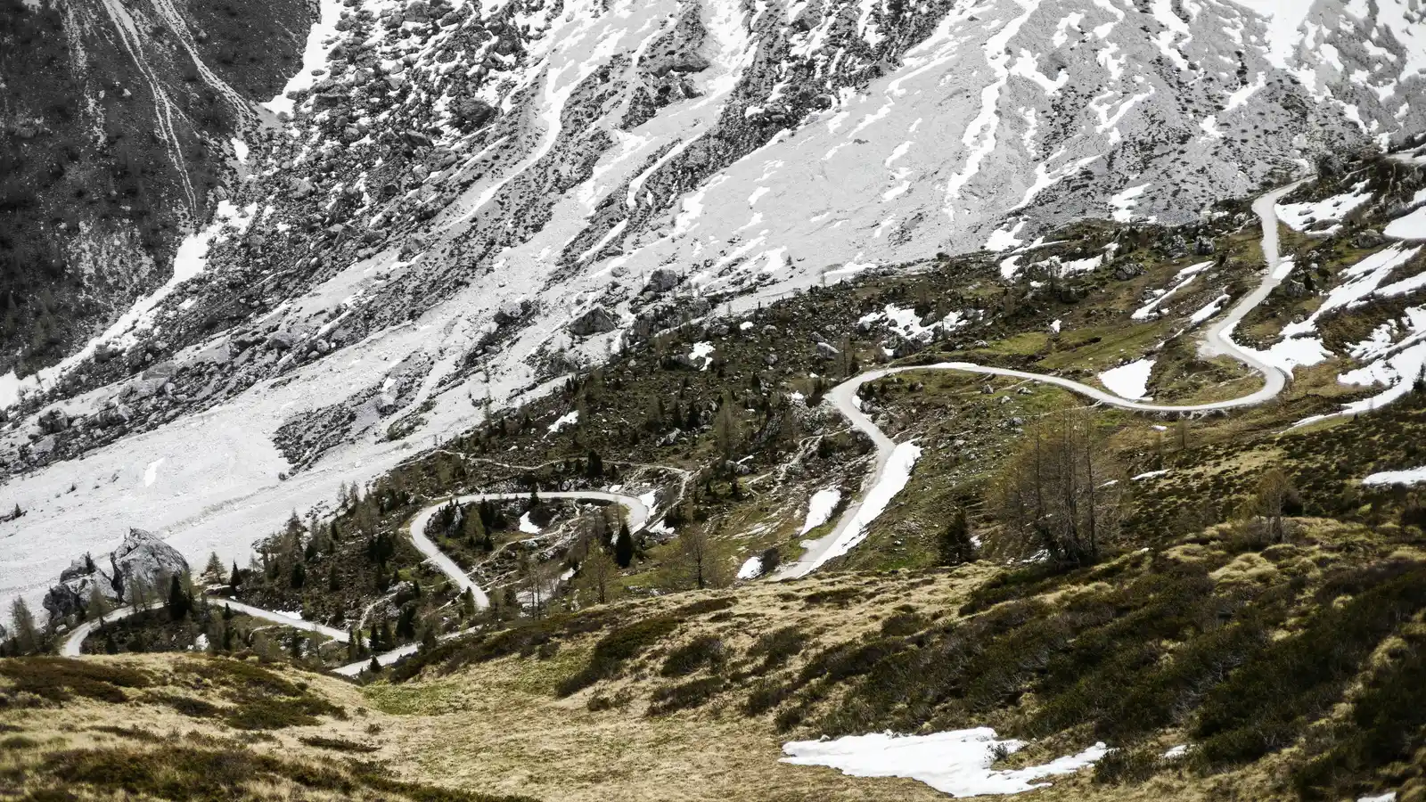 A road zigzagging up a mountainside with patches of snow